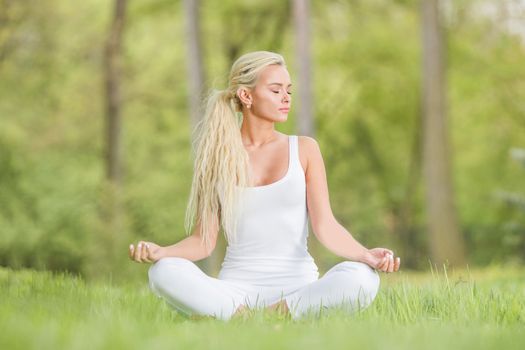 Yoga girl in lotus pose in the park, young woman in white clothes sitting on fresh green grass