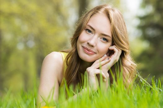 Happy smiling young woman laying on the green grass