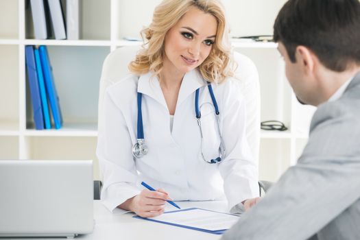 Patient and beautiful female doctor taking notes at medical clinic office