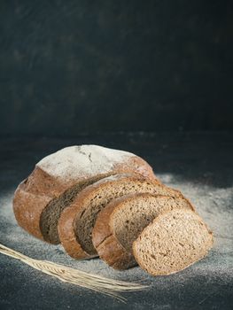 Sliced homemade sourdough rye bread with rye flour on black textured background. Copy space. Low key