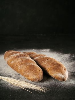 Two whole homemade rye loaf bread with buckwheat flour on black textured background. Copy space. Low key