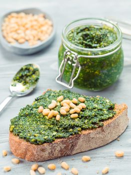 Close up view of whole grain rye bread with fresh basil pesto sauce on gray wooden table. Copy space.