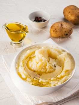 Mashed potatoes in white bowl with cloth napkin, pepper and olive oil on textured concrete white background