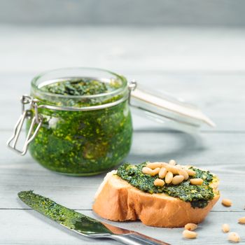 Close up view of baguette bread with fresh basil pesto sauce on gray wooden table. Copy space.