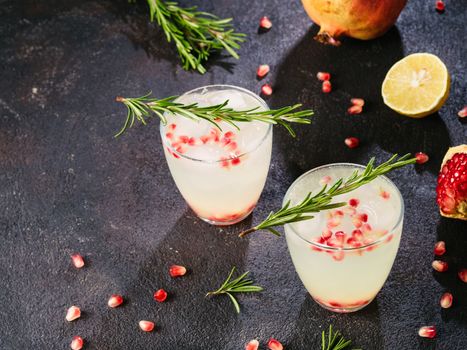 Autumn and winter cocktails idea - white sangria with rosemary, pomegrante and lemon juice and ingredients on black cement background. Copy space.