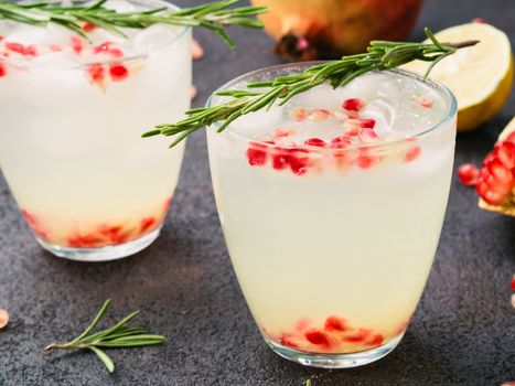 Autumn and winter cocktails idea - white sangria with rosemary, pomegrante and lemon juice and ingredients on black cement background.