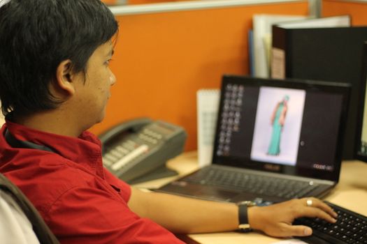 Office workers in a red shirts working in an office in orange cluster in the front of computer and laptop