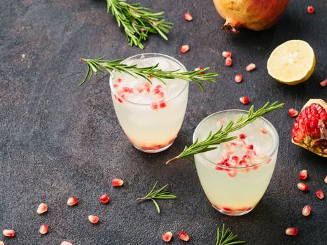 Autumn and winter cocktails idea - white sangria with rosemary, pomegrante and lemon juice and ingredients on black cement background. Copy space.