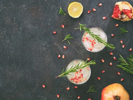 Autumn and winter cocktails idea - white sangria with rosemary, pomegrante and lemon juice and ingredients on black cement background. Copy space. Top view or flat-lay.