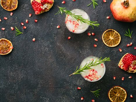 Autumn and winter cocktails idea - white sangria with rosemary, pomegrante and lemon juice and ingredients on black cement background. Copy space. Top view or flat-lay.