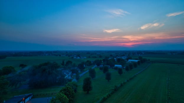 Aerial view of a summer sunset over farm lands with blue skies and red sun