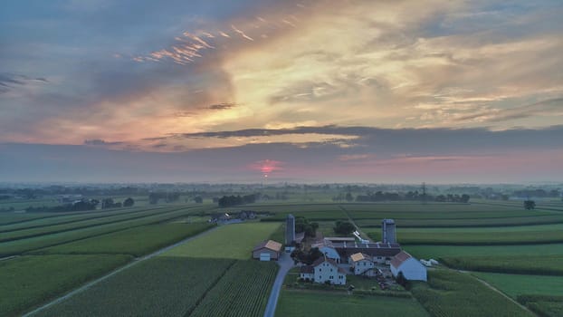 Aerial view of a summer sunset over farm lands with blue skies and red sun