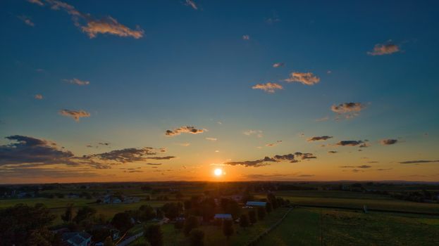 Sunset over barns, silos and green farmlands with blue, red and orange skies and a few clouds