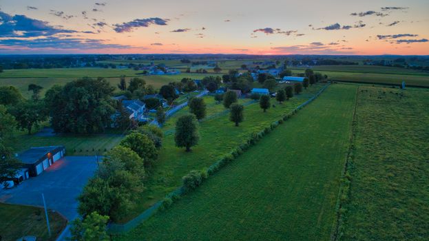 Sunset over barns, silos and green farmlands with blue, red and orange skies and a few clouds
