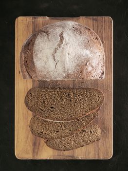 Sliced homemade sourdough rye bread on cutting board over black textured background with rye flour. Top view or flat-lay. Low key