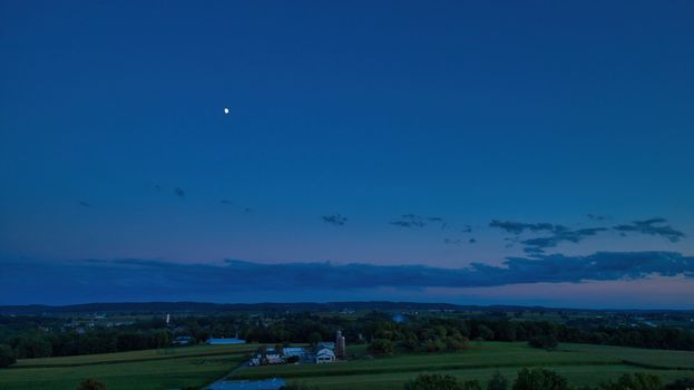 Sunset over barns, silos and green farmlands with blue, red and orange skies and a few clouds