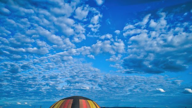 Aerial view of blue sky and multiple clouds and a hot air balloon floating thru it