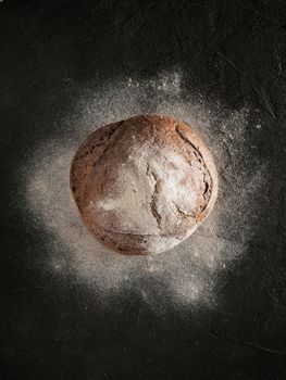 Whole homemade rye bread with rye flour on black textured background. Top view or flat-lay. Low key