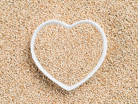 Quinoa in heart-shaped bowl on quinoa background. Gluten free ancient grain for healthy diet. I love quinoa concept. Copy space.