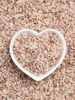 Red rice in heart-shaped bowl on rice background. Copy space. Top view or flat lay.