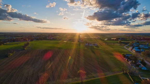 Aerial view of a Sunset over barns, silos and farmlands during the golden hour with blue sky, clouds and red sun