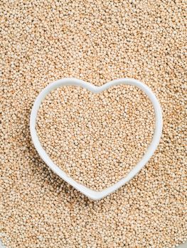 Quinoa in heart-shaped bowl on quinoa background. Gluten free ancient grain for healthy diet. I love quinoa concept. Copy space.