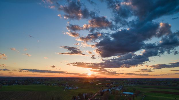 Aerial view of a Sunset over barns, silos and farmlands during the golden hour with blue sky, clouds and red sun