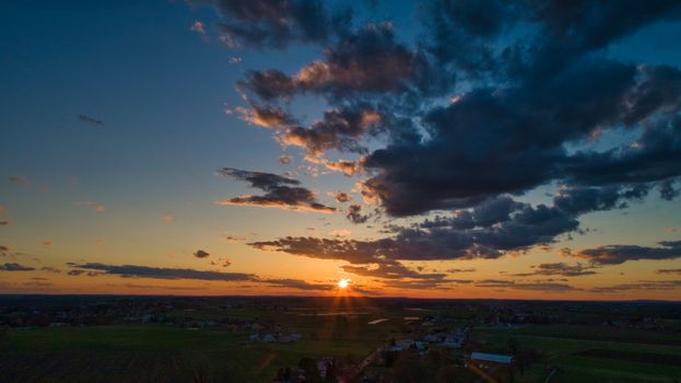 Aerial view of a Sunset over barns, silos and farmlands during the golden hour with blue sky, clouds and red sun