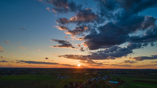 Aerial view of a Sunset over barns, silos and farmlands during the golden hour with blue sky, clouds and red sun