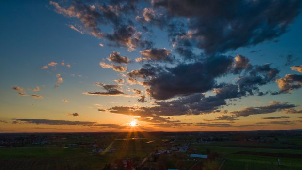 Aerial view of a Sunset over barns, silos and farmlands during the golden hour with blue sky, clouds and red sun