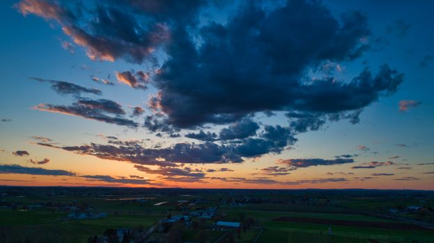 Aerial view of a Sunset over barns, silos and farmlands during the golden hour with blue sky, clouds and red sun