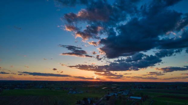 Aerial view of a Sunset over barns, silos and farmlands during the golden hour with blue sky, clouds and red sun