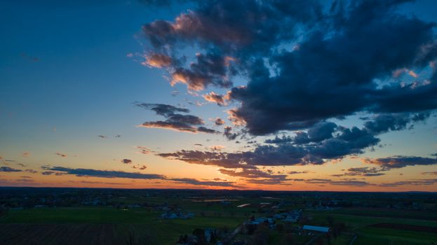 Aerial view of a Sunset over barns, silos and farmlands during the golden hour with blue sky, clouds and red sun