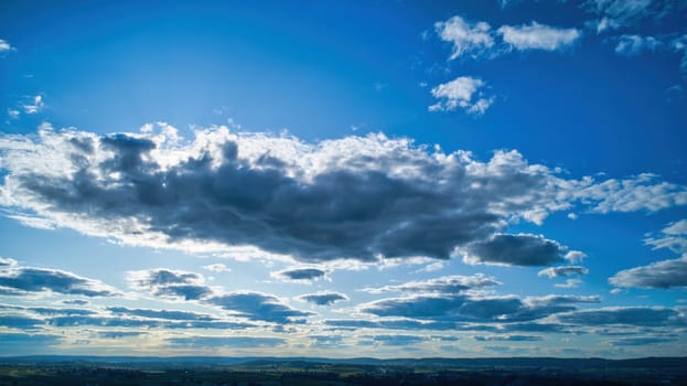 Blue sky and multiple clouds background showing a horizon and a hidden sun