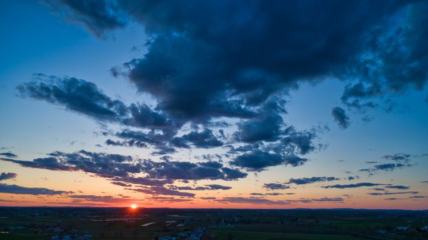 Aerial view of a Sunset over barns, silos and farmlands during the golden hour with blue sky, clouds and red sun