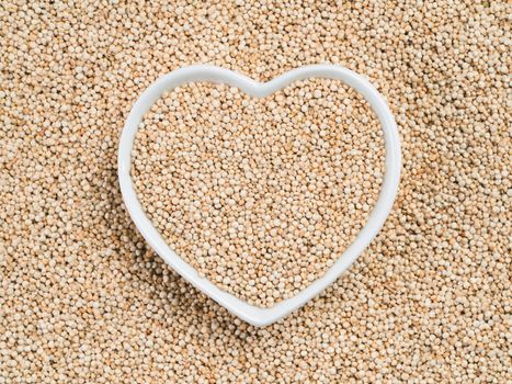 Quinoa in heart-shaped bowl on quinoa background. Gluten free ancient grain for healthy diet. I love quinoa concept. Copy space.