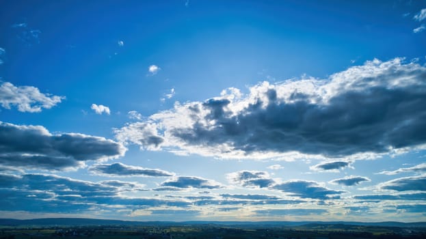 Blue sky and multiple clouds background showing a horizon and a hidden sun