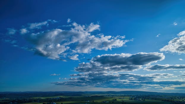 Blue sky and multiple clouds background showing a horizon and a hidden sun