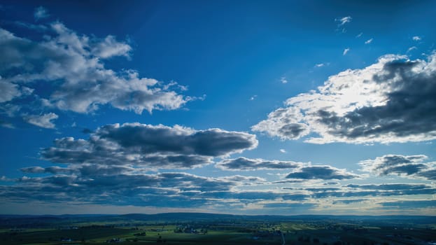 Blue sky and multiple clouds background showing a horizon and a hidden sun