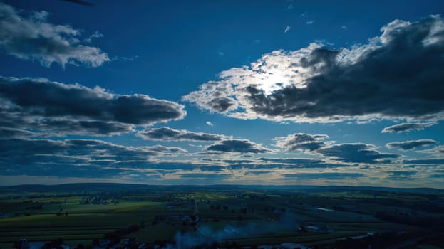 Blue sky and multiple clouds background showing a horizon and a hidden sun