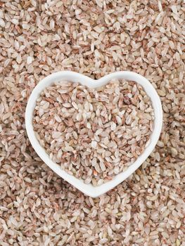 Red rice in heart-shaped bowl on rice background. Copy space. Top view or flat lay.