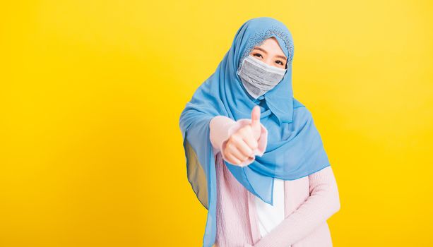 Asian Muslim Arab, Portrait of happy beautiful young woman religious wear veil hijab smiling she show finger thumb up for a good sign, studio shot isolated yellow background with copy space