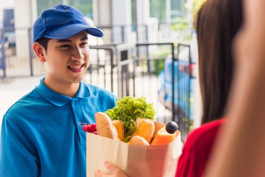 Asian young delivery man in uniform making grocery fast service giving fresh food in paper bag to woman customer receiving at house door under pandemic coronavirus, Back to new normal concept