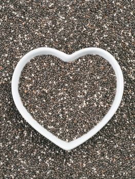 Heart-shaped bowl of chia seeds on chia background. Gluten free and healthy diet. I love chia seeds concept. Copy space.