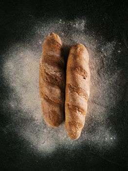 Two whole homemade buckwheat loaf bread with buckwheat flour on black textured background. Top view or flat-lay. Low key