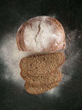 Sliced homemade sourdough rye bread with rye flour on black textured background. Top view or flat-lay. Low key