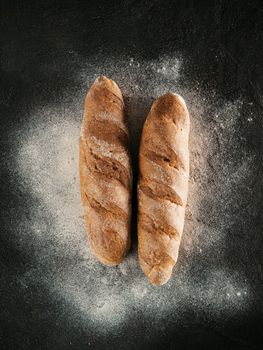 Two whole homemade buckwheat loaf bread with buckwheat flour on black textured background. Top view or flat-lay. Low key