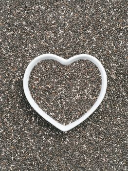 Heart-shaped bowl of chia seeds on chia background. Gluten free and healthy diet. I love chia seeds concept. Copy space.