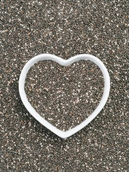 Heart-shaped bowl of chia seeds on chia background. Gluten free and healthy diet. I love chia seeds concept. Copy space.