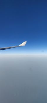 Airplane wing seen from the window of the airplane amidst blue sky and above clouds